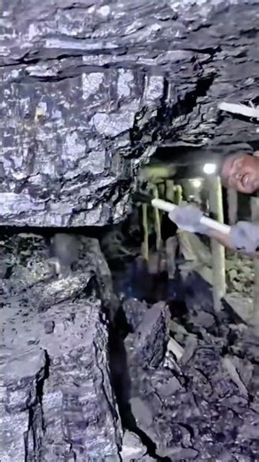 digging coal in a deep underground mine with a shovel and a headlamp to harvest natural resources