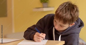 A teenage student is engaged in studying and notetaking in a classroom, showing deep concentration and thoughtfulness