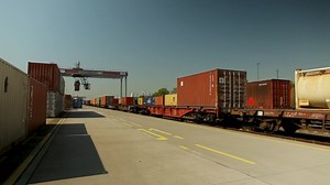 Premium stock video - Freight train with colorful containers at a commercial dock during daytime, clear blue sky