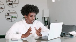 African American hipster ethnic guy student using laptop talking to web cam learning english online on virtual elearning class or having hybrid video call job interview meeting sitting at home table.