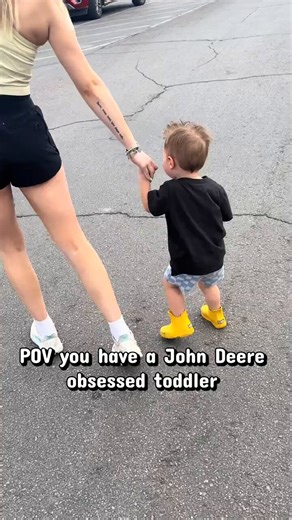 This little blonde toddler in yellow boots walks through the parking lot holding his mom’s hand then climbs onto a giant green John Deere riding mower on display.He grabs the steering wheel smiles big and pretends to drive while sipping from a bottle as the full lineup of tractors sits behind him.You watch a tiny kid completely obsessed with John Deere equipment turn a simple store stop into his personal playground. Do you think it is cute and the kind of innocent passion every parent should enc