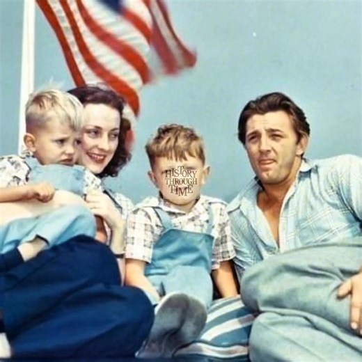 "Robert Mitchum and his wife, Dorothy, enjoy a serene afternoon at their California home in 1949, joined by their young sons, James and Christopher. At this point in his career, Mitchum was already a celebrated star, known for his charismatic performances in film noir classics and Westerns. Away from Hollywood sets, the couple embraced a quiet, family-centered life, with their home becoming a haven from the industry’s constant demands. This rare glimpse into their personal world captures the war