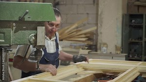 A worker is lining up the wooden frame for the window drilling process. A laborer is using the industrial equipment for the window drilling process. Window drilling process at the carpentry plant.
