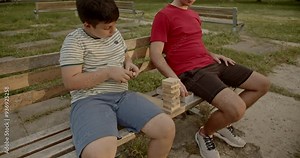 Two brothers sitting on a park bench, preparing for a building blocks game. They are having fun and spending their free time together.