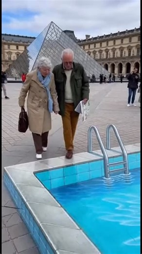 Badi | Ai Creator | An elderly couple with gray hair, both over 70, carefully approaches a large 3D illusion on a public square. The illusion looks like a deep... | Instagram