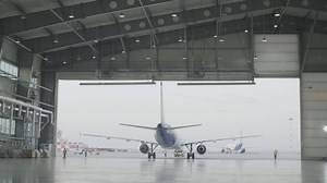 Airplane parking in the airport hangar. Airplane in hangar, rear view of aircraft and light from windows. Roll-out of the aircraft from the hangar by a tractor, after repair