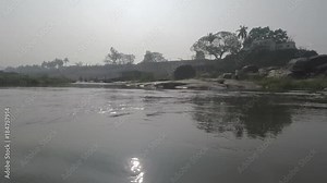 Crossing river in Hampi, India. Smooth shot passes Shiva lingams in water, islands, grass, and men bathing an elephant. 2X slow motion.