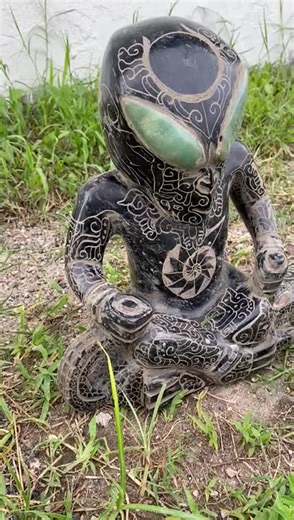 This extraordinary sculpture appears to represent a cosmic or extraterrestrial being in a meditative state, fusing advanced symbolism, Mesoamerican artistry, and otherworldly iconography. Below is a symbolic and fictional translation of what this piece might represent:The being sits in the ancient lotus position — a posture of deep meditation, equilibrium, and transcendence. This represents a timeless connection between Earthly mystics and interdimensional travelers. The pose suggests the being 