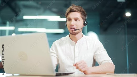 customer service support agent sits in modern office communicates online with a headset. Man specialist manager working in laptop computer. Handsome young Caucasian male telemarketing and consulting