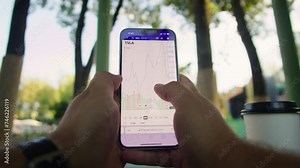 Young woman holding and swiping phone with stocks graphis in front of trees in the park close-up. Business woman searching economic charts on smart phone. Nature