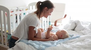 Young mom, changing baby diaper after bath in sunny bedroom