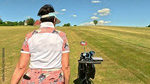 Mature woman playing golf. Female golfer walking on golf course with automatic electric golf cart. Beautiful sunny landscape, with green hills and blue sky.