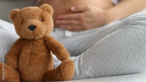 Pregnancy. Pregnant woman wearing maternity clothes relaxing on home sofa with teddy bear baby toy in focus for baby shower gift concept or expecting a child