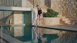 Young woman tests the water with her toe in swimming pool. Luxury holiday