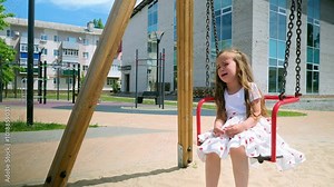 Upset crying baby girl on the playground at swing. Children playing outdoor, kids outside, summer holiday and vacation