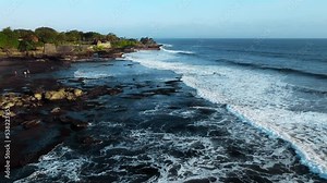 A view from a drone flying over the sea with waves and shore views with clouds above and rocks below.