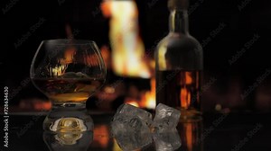 Glass of cognac with ice stands on a table against background of a fireplace with a flame