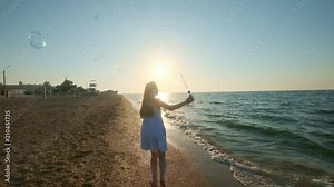 Girl blowing bubbles on beach in slow motion. A young girl blows soap bubbles in the evening, during sunset. Runs along the beach, soap bubbles fly in the sunlight Stock Video
