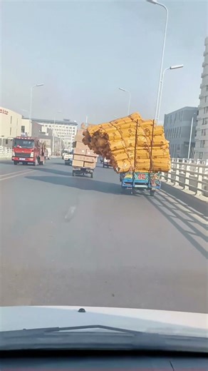 Overloaded Three-Wheeled Truck on Urban Highway, Yellow Goods Tilted at a Dangerous Angle!