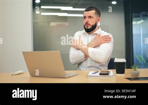 Bearded man in white shirt feeling cold at office desk, rubbing his arms and shoulders. Male executive using air conditioner remote control to increase heating in workspace Stock Video Footage - Alamy