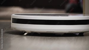 A robot hoover cleans the floor from dust. The device moves to the camera and goes into defocus. Close-up. Low angle of shooting. Automatic house cleaning. Slow motion