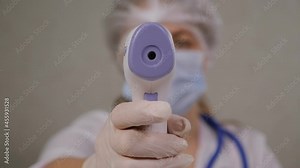 Young female doctor in uniform is measuring your body temperature with a digital infrared thermometer.