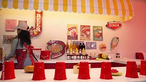 Professional hispanic restaurant worker dancing and standing behind food bar. Attractive waitress with red apron moving to freestyle music while looking at camera. Crazy and funny dance. Regalement.