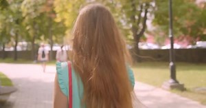 Closeup back view portrait of young pretty female walking turning and looking at camera with flattering hair smiling happily in park