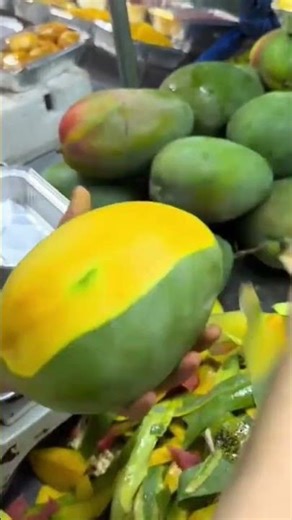 peeling a fresh large green mango using manual handheld metal peeler for efficient fruit preparation