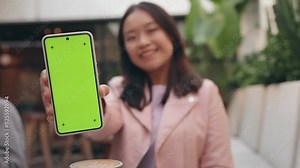 Cheerful Asian woman displaying a smartphone with a green screen and tracking points, ideal for mobile app mockups.