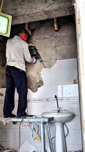 Removing wall plaster using power tool on scaffold