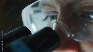 Extreme close-up view of eyes of female scientist wearing protective goggles intently looking into a microscope when performing research in laboratory