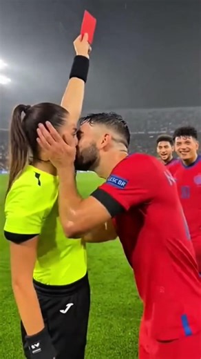 female referee halts the match and firmly raises a red card toward a male player