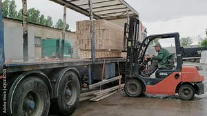 A forklift unloads wooden boards , moving while approaching the goods to unload it while raining.
