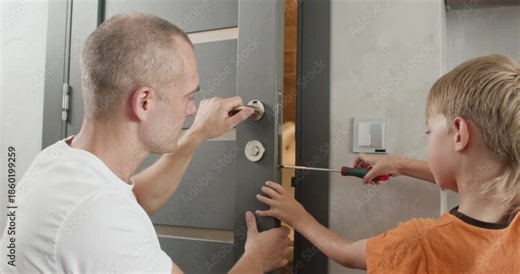 Attentive father supports curious son during simple door handle installation task. Safe hands-on learning develops practical skills in home repairment