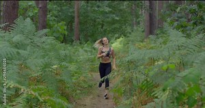 Pretty Blonde Young Woman jogging toward Camera in Forest. Active Girl in Headphones and Gym Top. Sporty Lady in British Wood on a Summers Day