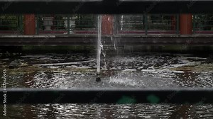 View a fountain on the lake with ducks and lotus leaves floating on the water bounded by railing on all sides on the grounds of Excellency Midlands Wedding Venue.Fountain causing ripples on the water.