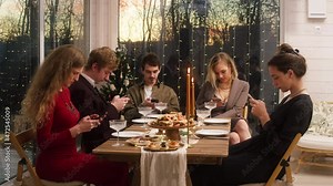 People using smartphones, sitting at dining table. Friends celebrating new year at home, chatting in phones. Boring christmas party concept, festive dinner.
