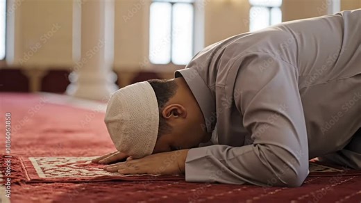 Medium close-up from behind of a man bowing low in a sujud position. Focus on the plush fabric texture of the prayer mat and soft contours of a white head covering 4K