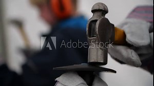 A slow motion closeup shot of children learning how to use a hammer and chisel. The hammer smacks the chisel head hard and the chisel has a safety grip to prevent any accidents occurring