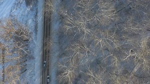 Above view of white SUV going on a snow covered forest road. Car rides at icy woods route at winter time. Auto driving over beautiful nature way. Concept of travel and active weekends. Aerial shot