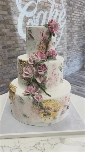 This stunning three-tier cake boasts hand-crafted edible flowers, intricate detailing, and gold leaf accents for a sophisticated finish. Each petal is meticulously sculpted by hand. #sculptedflowers #goldleafart