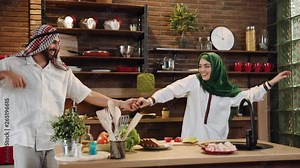 Funny young muslim couple cook together cut vegetables dance on kitchen smile talk at home food arab arabian arabic dinner eating emirates fresh happy healthy islam meal preparing slow motion