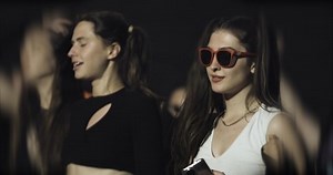 girls dancing in crowd in front of stage with flashing lights.