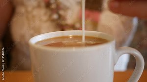 Woman puts cream into her coffee and stirs with spoon