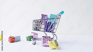 Multi-colored gift boxes fall into a shopping cart on a white background. 4k raw slow motion video 60 fps. Filmed on high speed cinema camera, 1000fps.