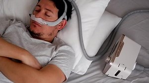 Close-up of healthy young adult man wearing under the nose nasal mask ( CPAP mask ) and using CPAP machine for sleeping smooth without snoring.
