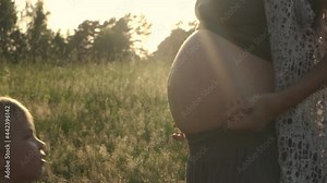 Little child boy older brother kissing pregnant mother belly on nature. Pregnancy woman outdoor on summer field on sunset. Authentic family moments of expecting baby.