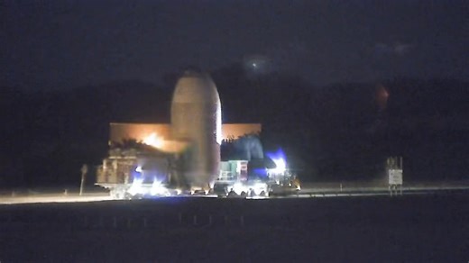 A Falcon 9 fairing headed down the road past the Vehicle Assembly Building on its trek up to SLC-40, as seen on our 24/7 livestream, Space Coast Live (link in the comments below. 👇) | NASASpaceflight.com