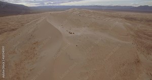 Top Of The Sand Dunes / Aerial 4K footage of people on top of an enormous sand dune with mountains in the background on a cloudy day.